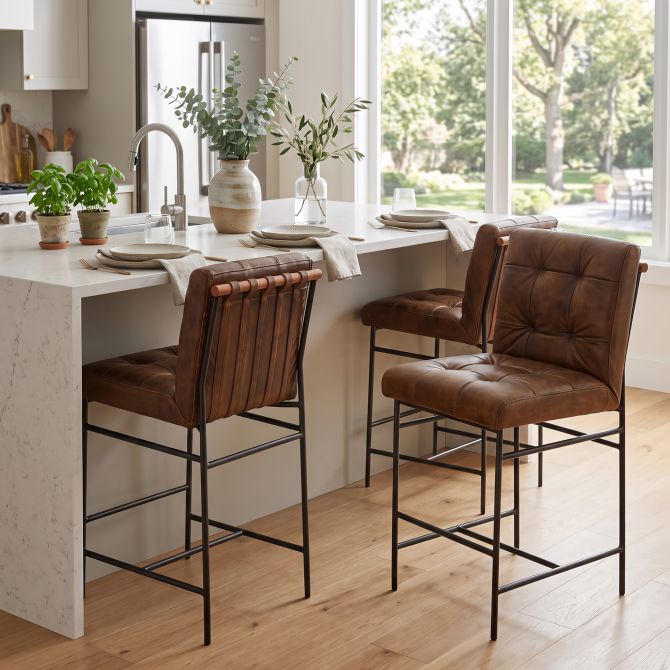 Brown leather tufted counter chairs with black iron frame in kitchen at white marble island
