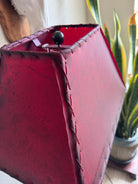 Close-up of a red leather lampshade with stitching details, blurred plant in the background