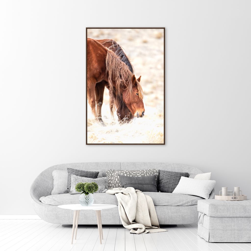 Framed canvas artwork of wild horses eating on a wall above a gray sofa in a living room.
