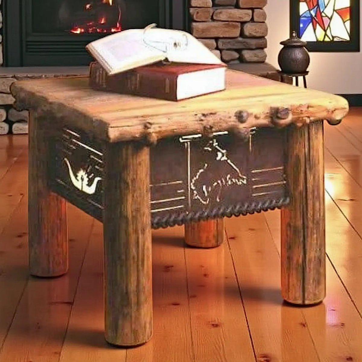 A rustic log-style end table with metal cutout bronc and western motifs, shown in a cozy room setting with a fireplace, books on top, and a wooden floor.