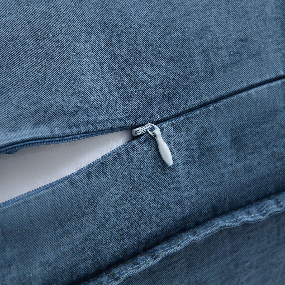 Close-up of a blue denim or canvas fabric item with a zipper opening, showing the texture of the material and a small white pull tab.